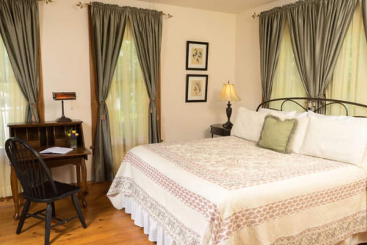 A bedroom with a bed, a desk, and a chair. There are two lamps on the nightstands.