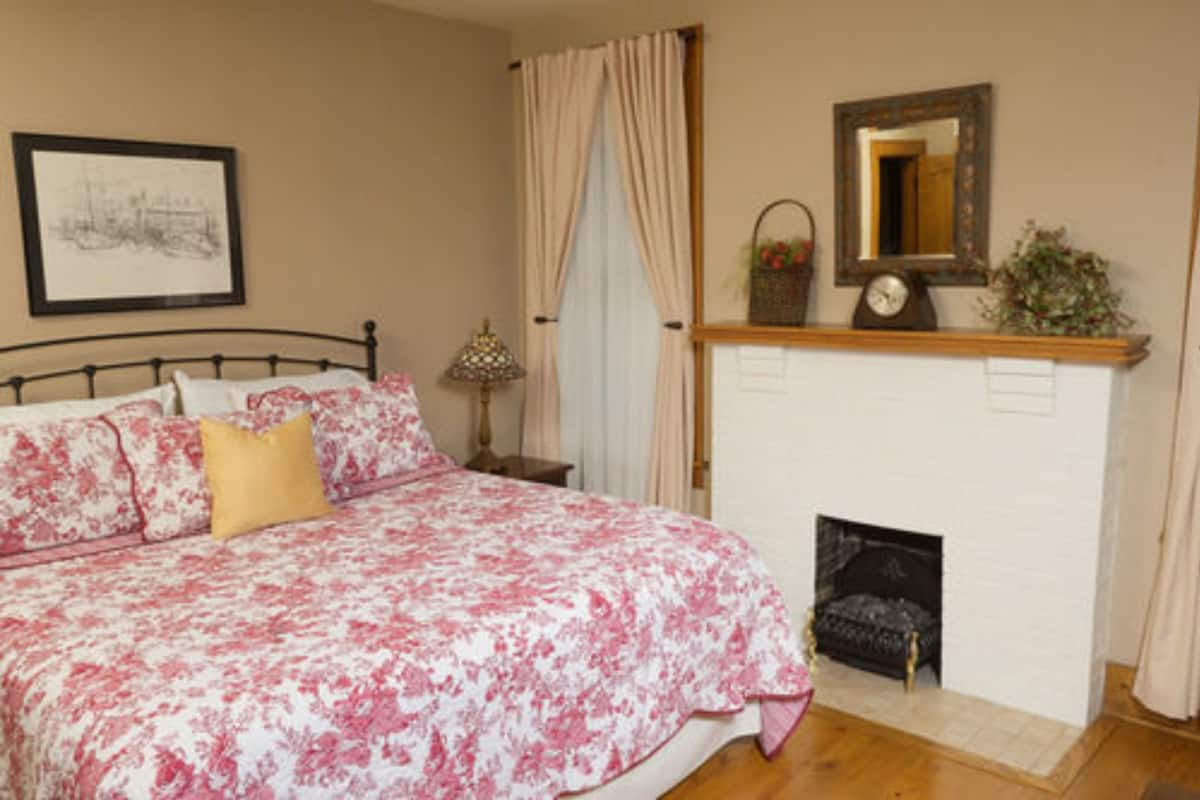 A bedroom with a bed, a nightstand, a lamp, a fireplace, and a mirror on the wall.