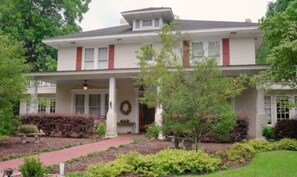 A two-story house with a covered porch, a front door, and a small garden with shrubs and a pathway.