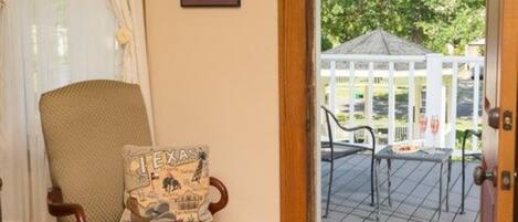 A room with a wicker chair and a door leading to an outdoor patio with a gazebo and a table.