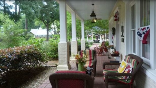 A covered porch with two wicker chairs, a table, and a hanging light fixture.