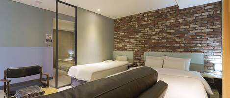 Una habitación de hotel con dos camas, un espejo grande, un sofá de cuero negro y una pared de ladrillo.