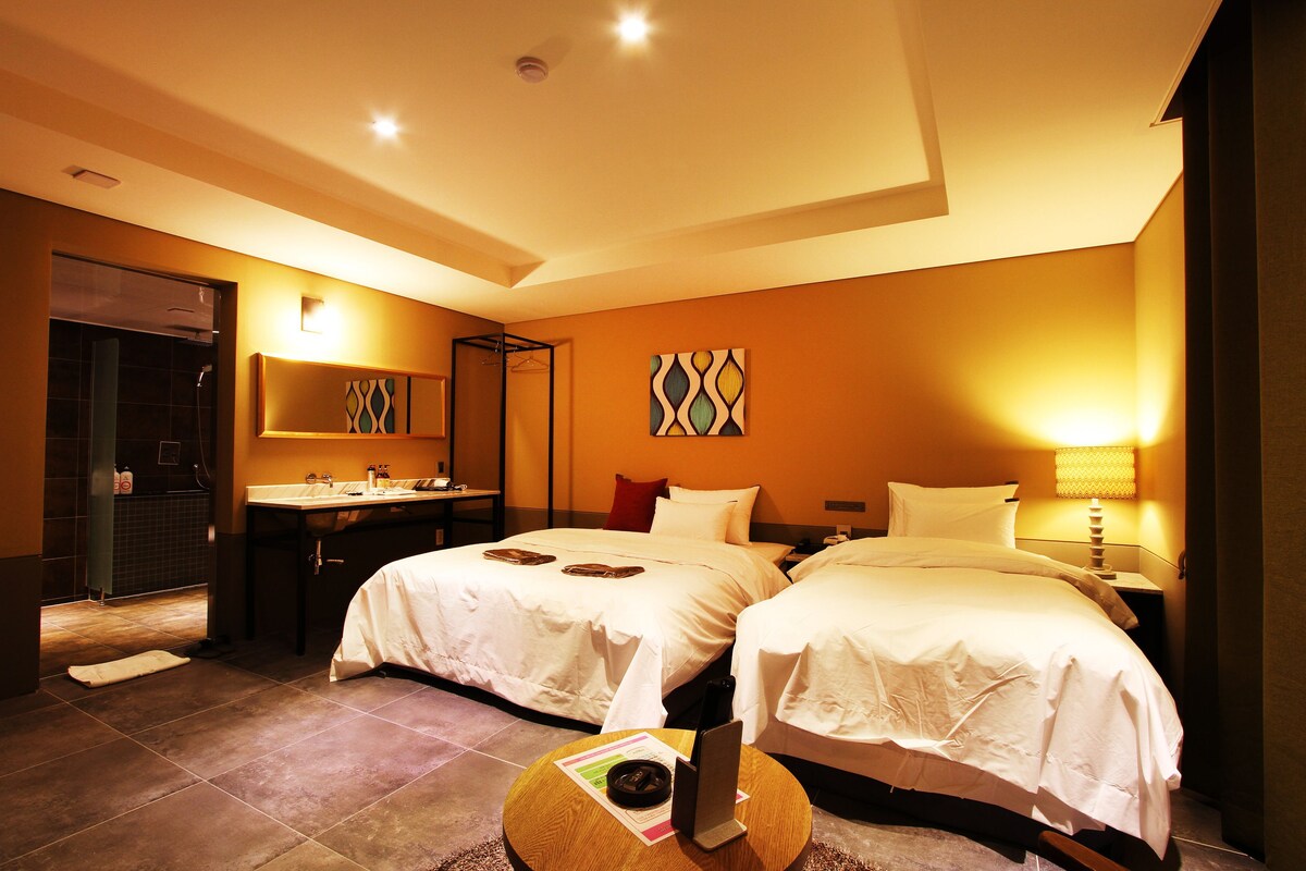 A hotel room with two beds, a bathroom, a desk, and a mirror.