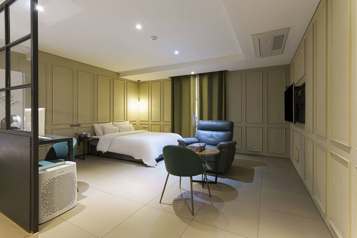 A hotel room with a bed, a desk with a computer, a chair, a TV, and a heater.