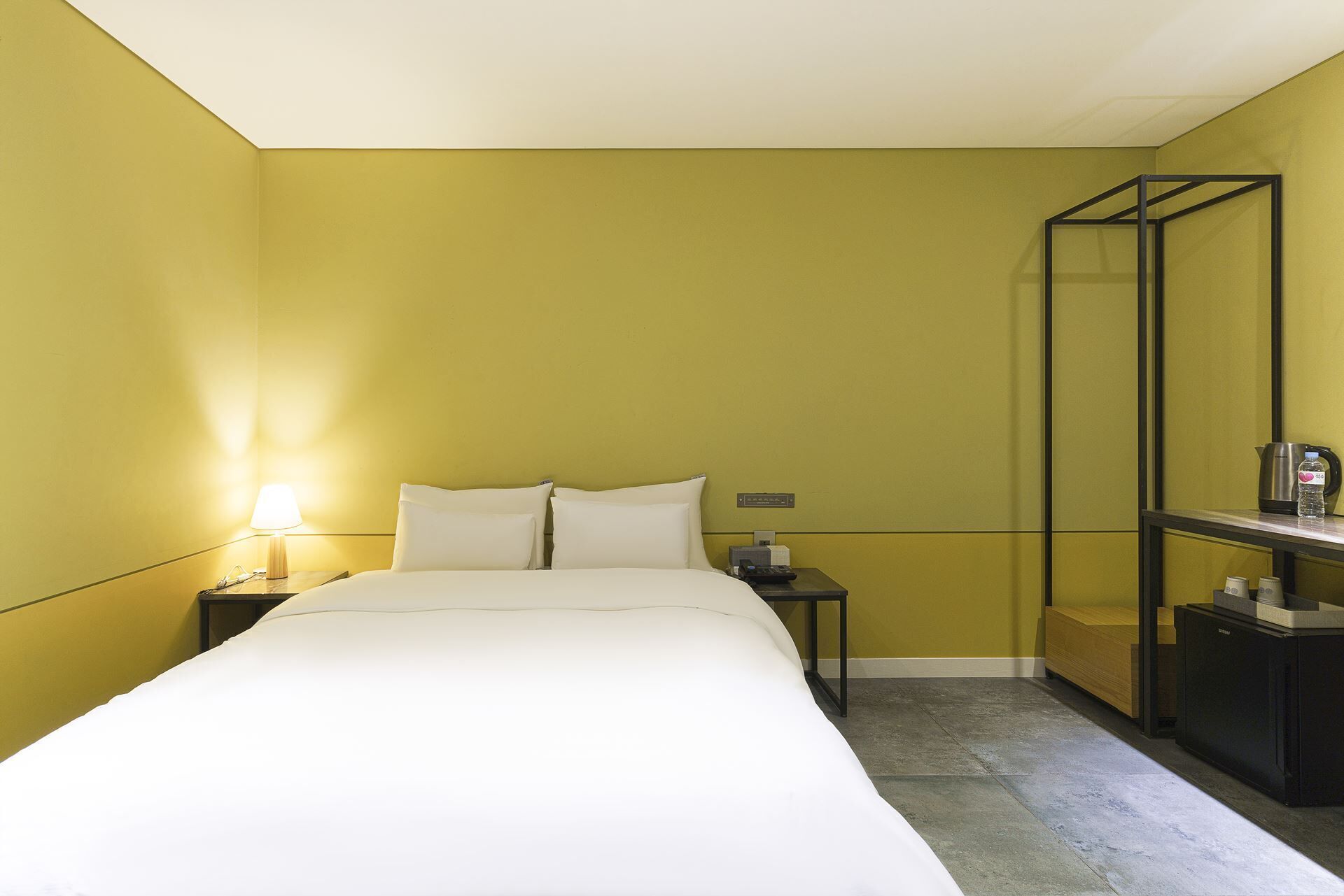 A hotel room with a bed, bedside table, lamp, and a small cabinet.