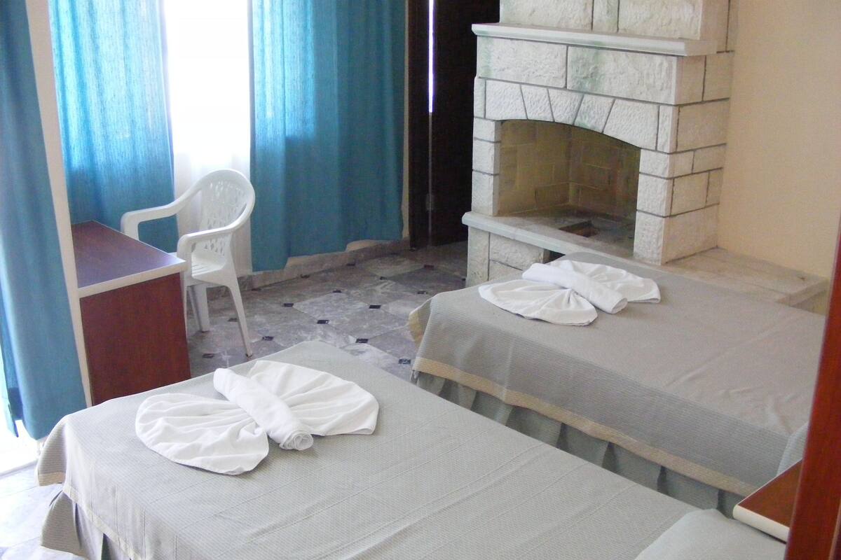 Una habitación de hotel pequeña con dos camas, un escritorio, una silla y una chimenea de piedra.