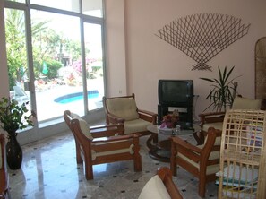 A living room with a pool view, wooden furniture, a television, and a decorative wall piece.