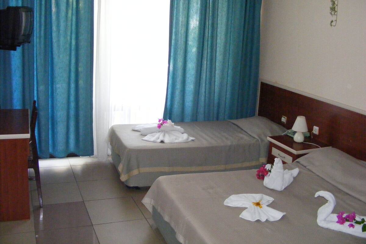 Habitación de hotel con dos camas, un escritorio, un televisor y una ventana con cortinas.