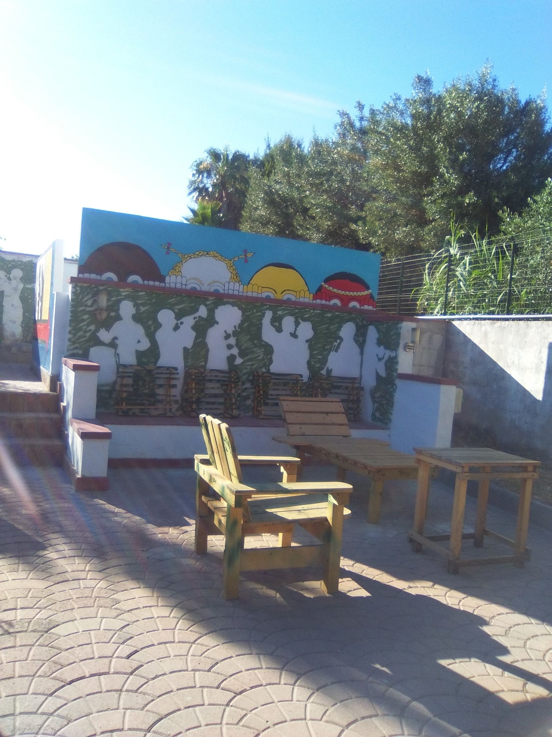 Uma área de estar ao ar livre com móveis de madeira e um mural na parede.