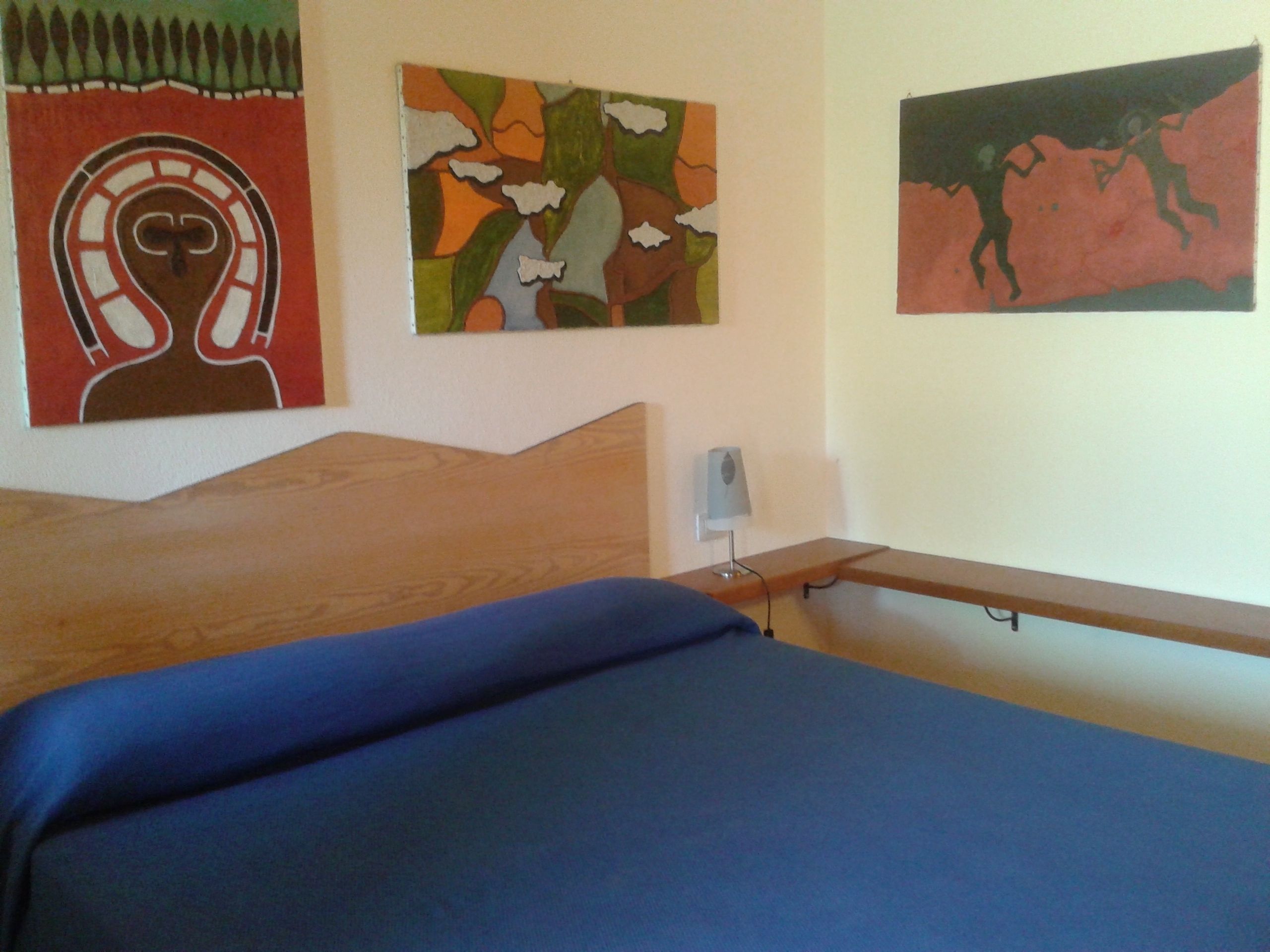 Una camera da letto con un letto di legno, un materasso blu e tre opere d'arte alle pareti.
