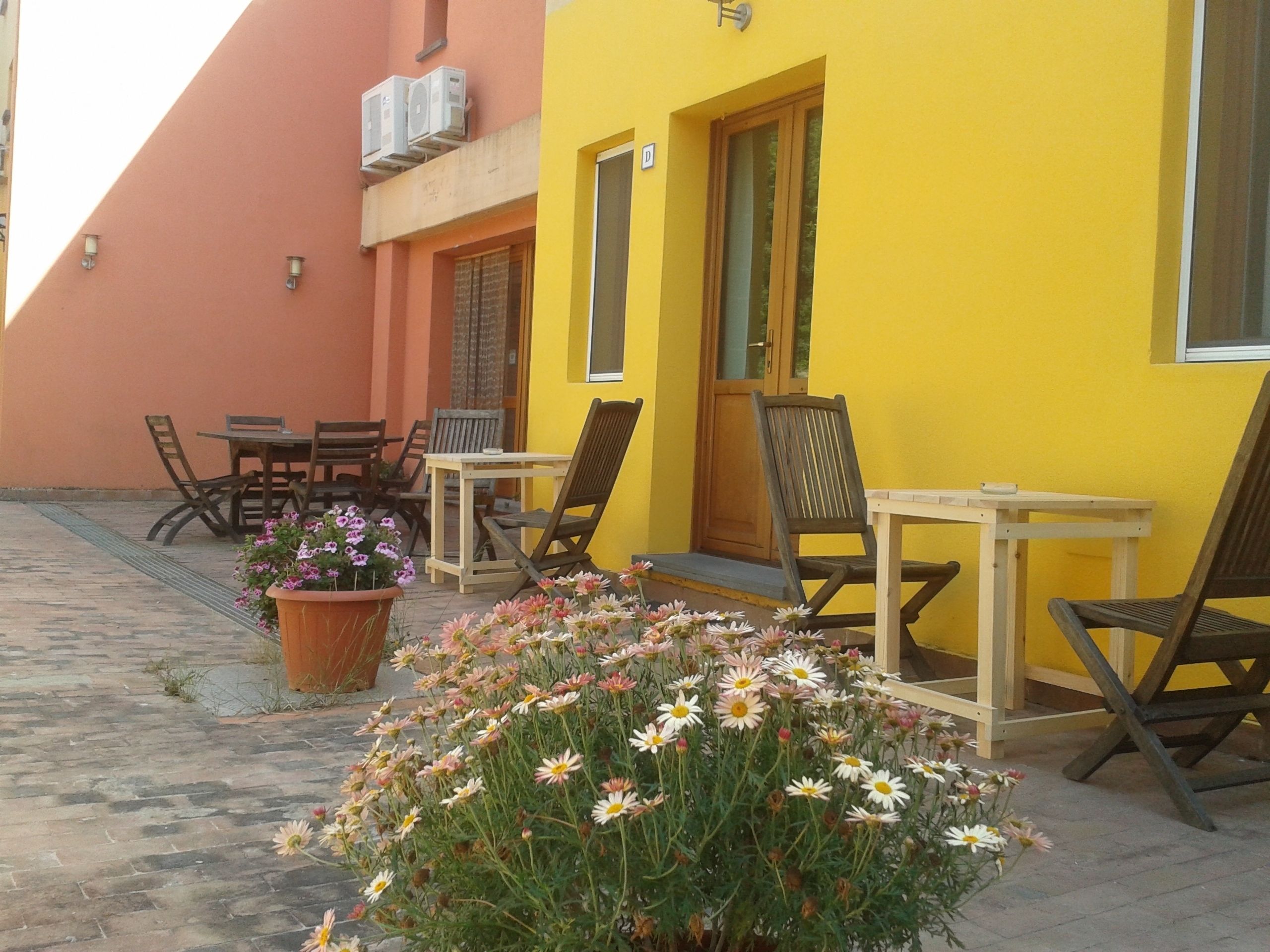 A yellow building with outdoor seating and a potted plant with flowers.