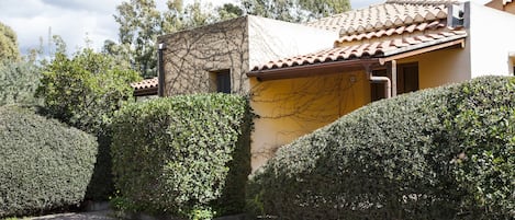 A building with a tiled roof and a yellow wall, surrounded by well-maintained hedges.