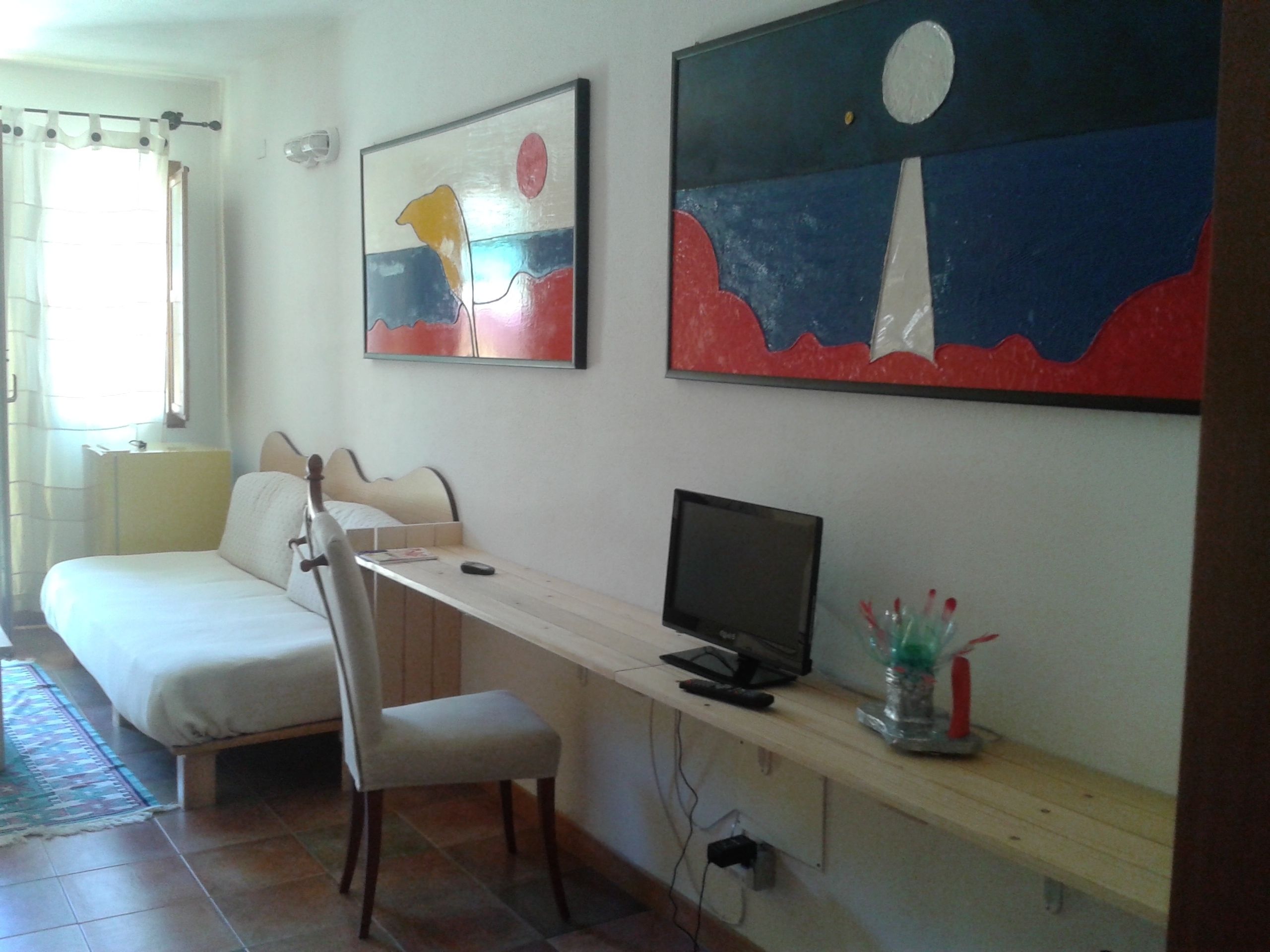 Ein Schlafzimmer mit einem Bett, einem Schreibtisch mit Computer und zwei Bildern an der Wand.