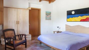 A bedroom with a bed, a wooden chair, a wardrobe, and a painting on the wall.