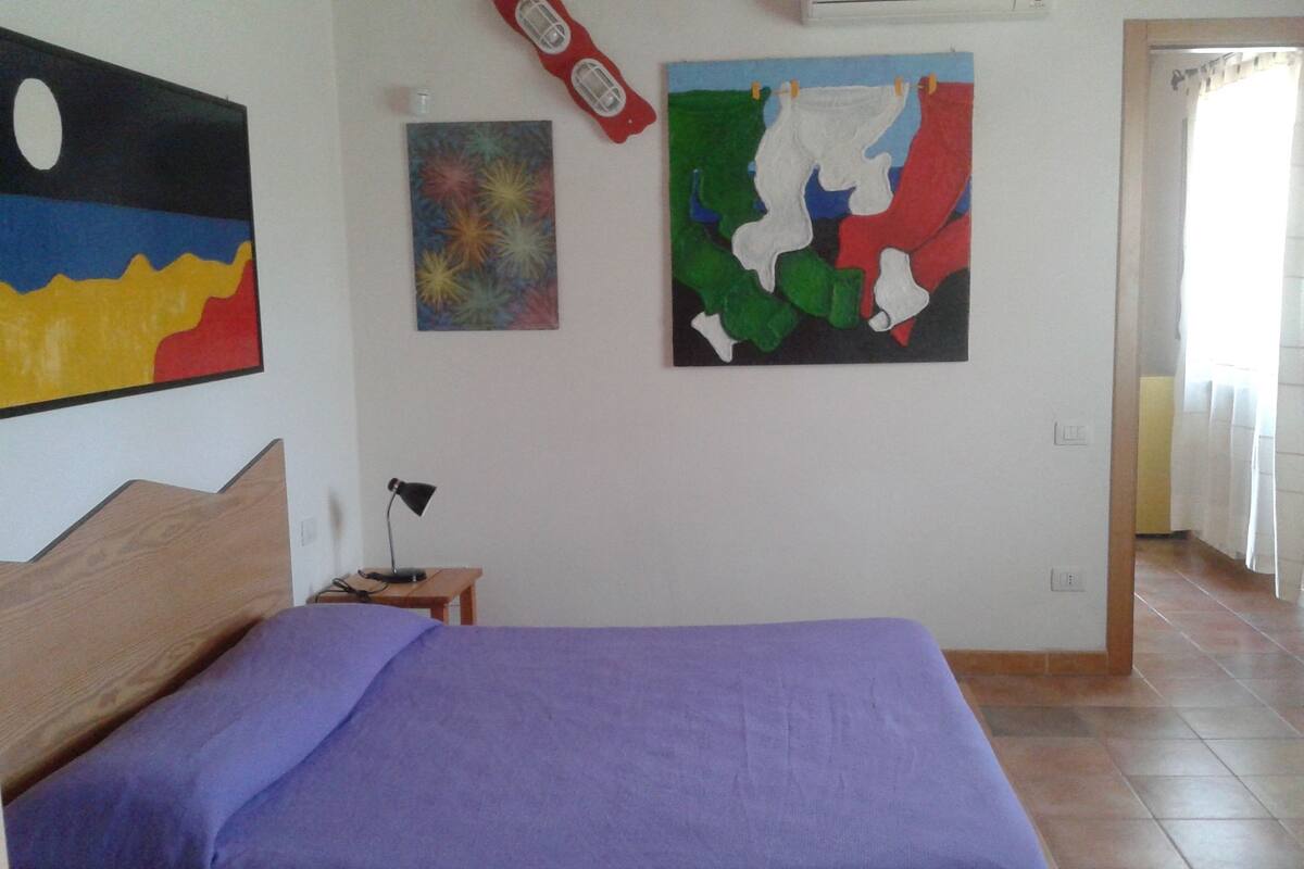 A bedroom with a bed, a desk, and two paintings on the wall.