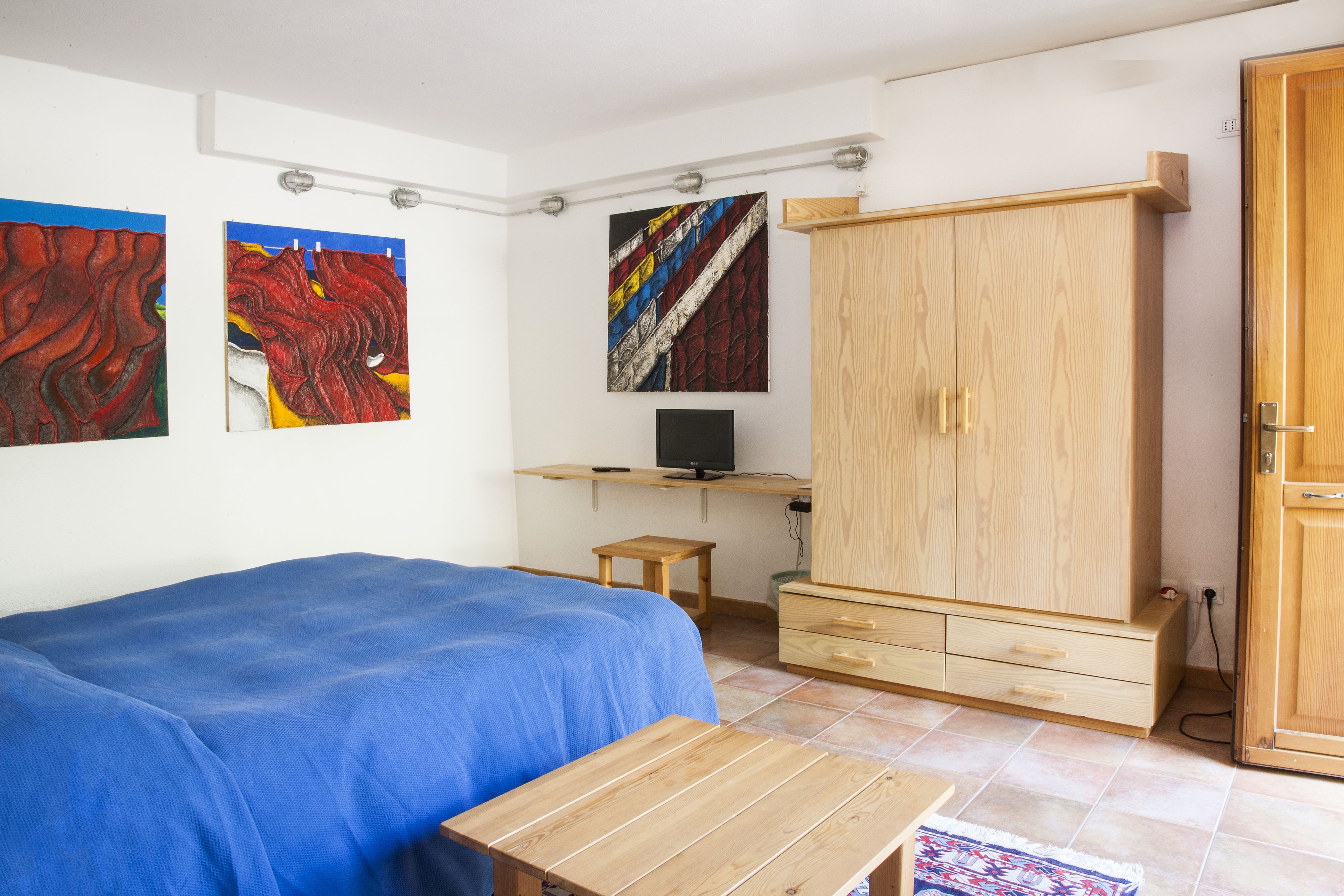 Un dormitorio con cama, escritorio, computadora, armario y obras de arte en la pared.