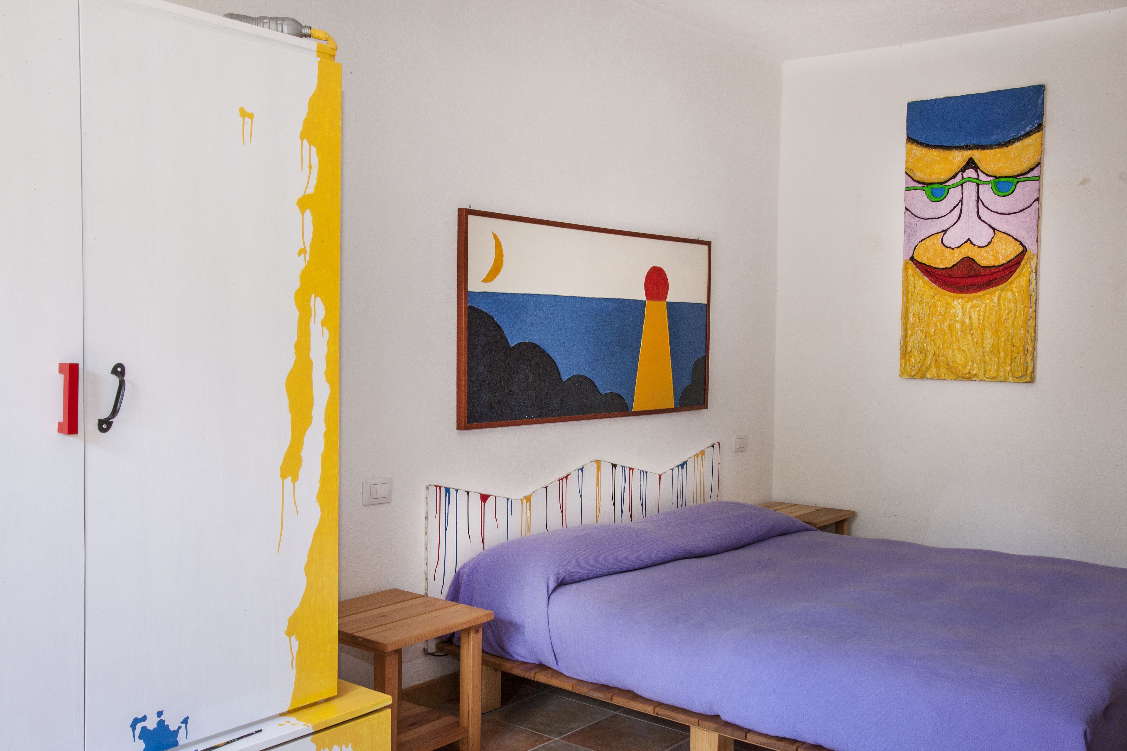 Un dormitorio con una cama, una mesita de noche de madera, un armario y dos cuadros en la pared.