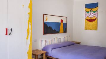 Un dormitorio con una cama, una mesita de noche de madera, un armario y dos cuadros en la pared.