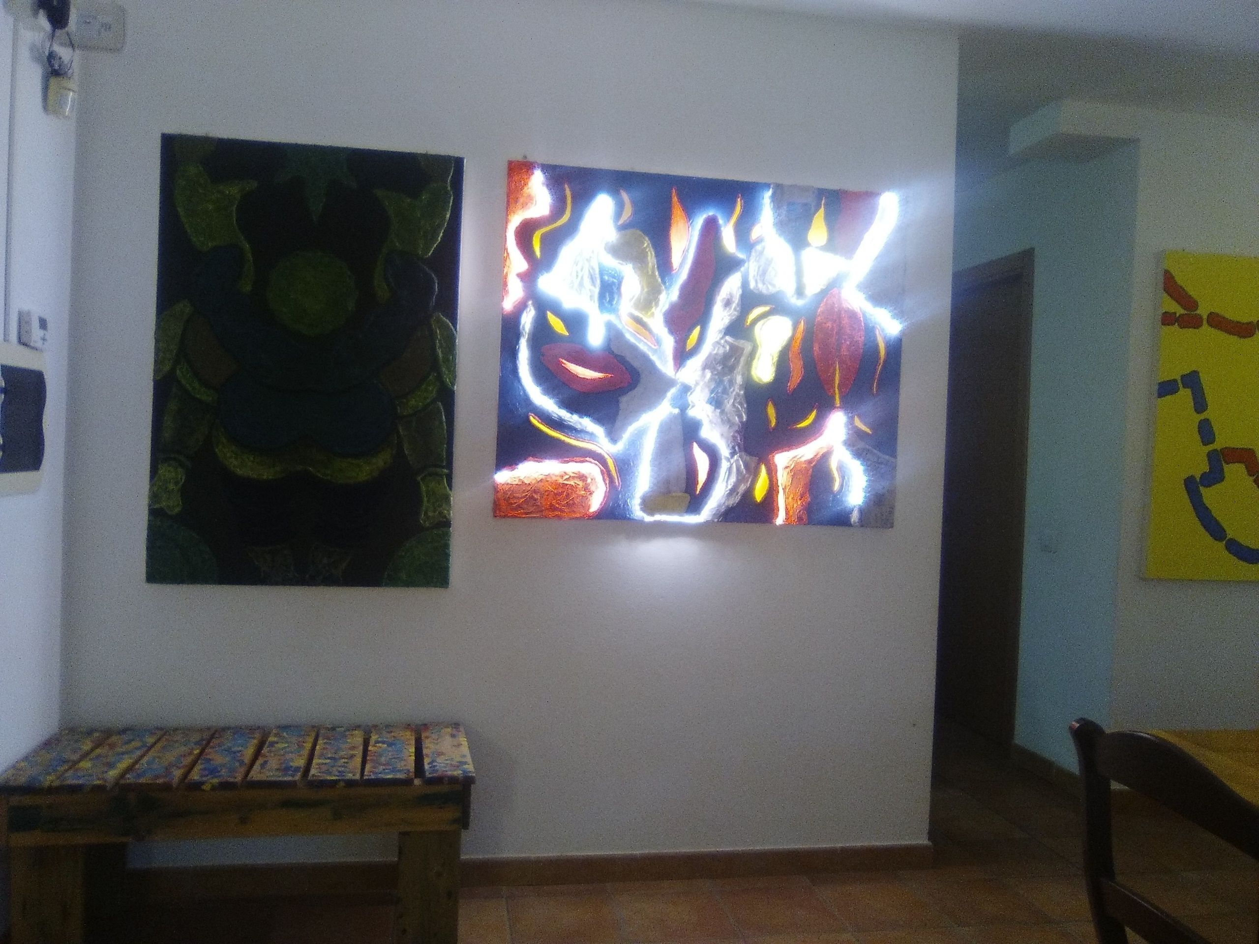 A room with two artworks on the wall, a small wooden table, and a chair.