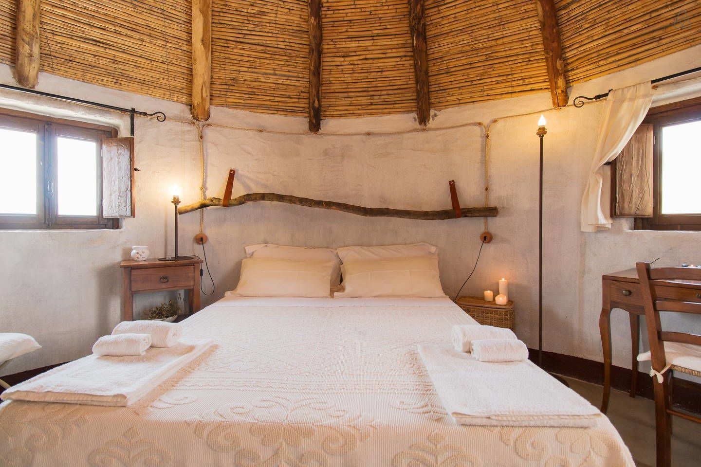 A cozy bedroom with a bed, bedside tables, a chair, and a hanging light fixture.