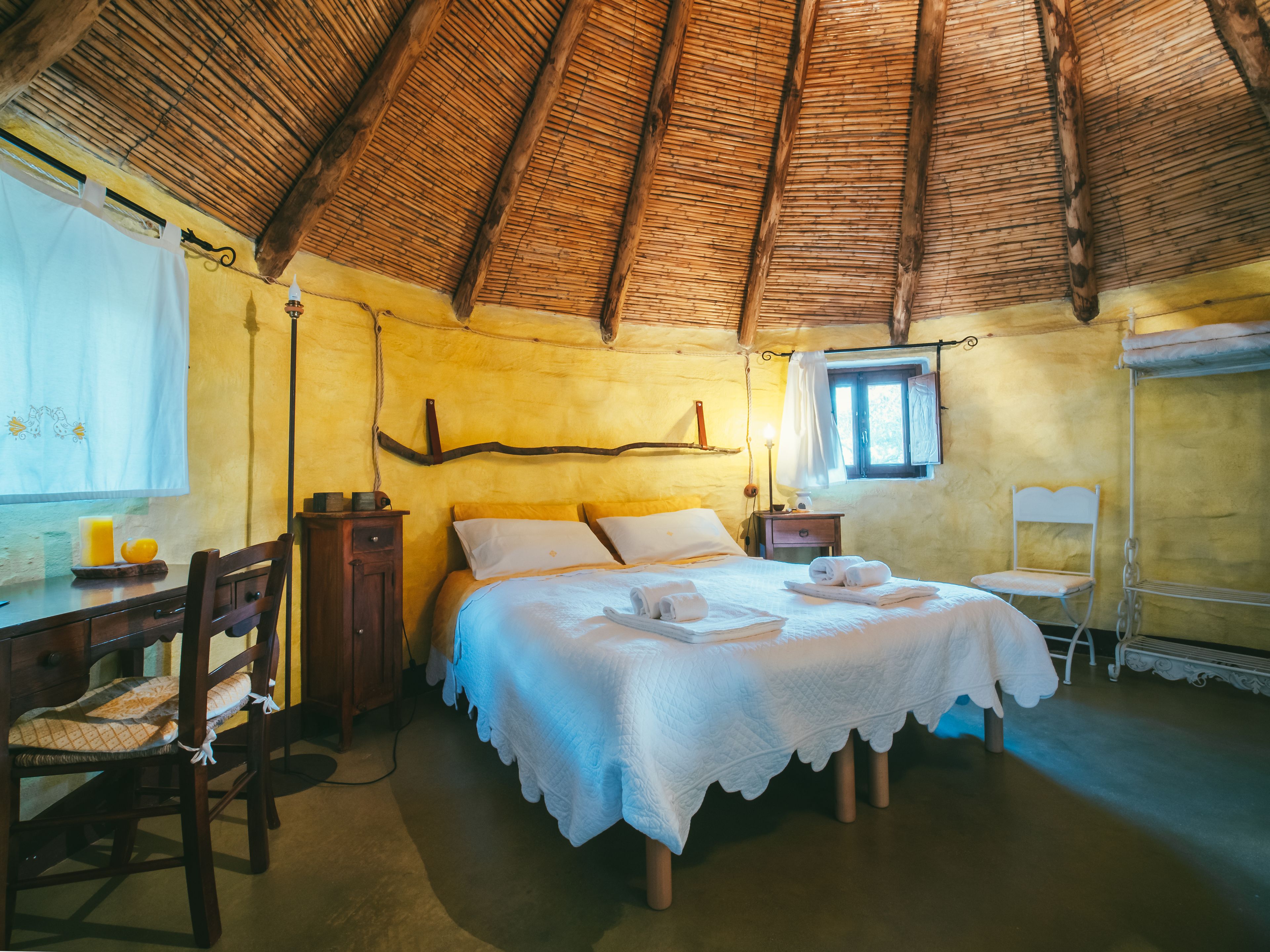 Una habitación acogedora con techo de madera, cama con ropa blanca, escritorio de madera y una silla.