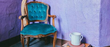 A vintage chair with a tufted backrest and a wooden base, positioned next to a small wooden table with a white cup on top.