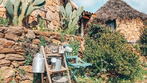 A rustic stone building with a thatched roof, surrounded by cacti and greenery. - Essenza Sardegna (Torpe)