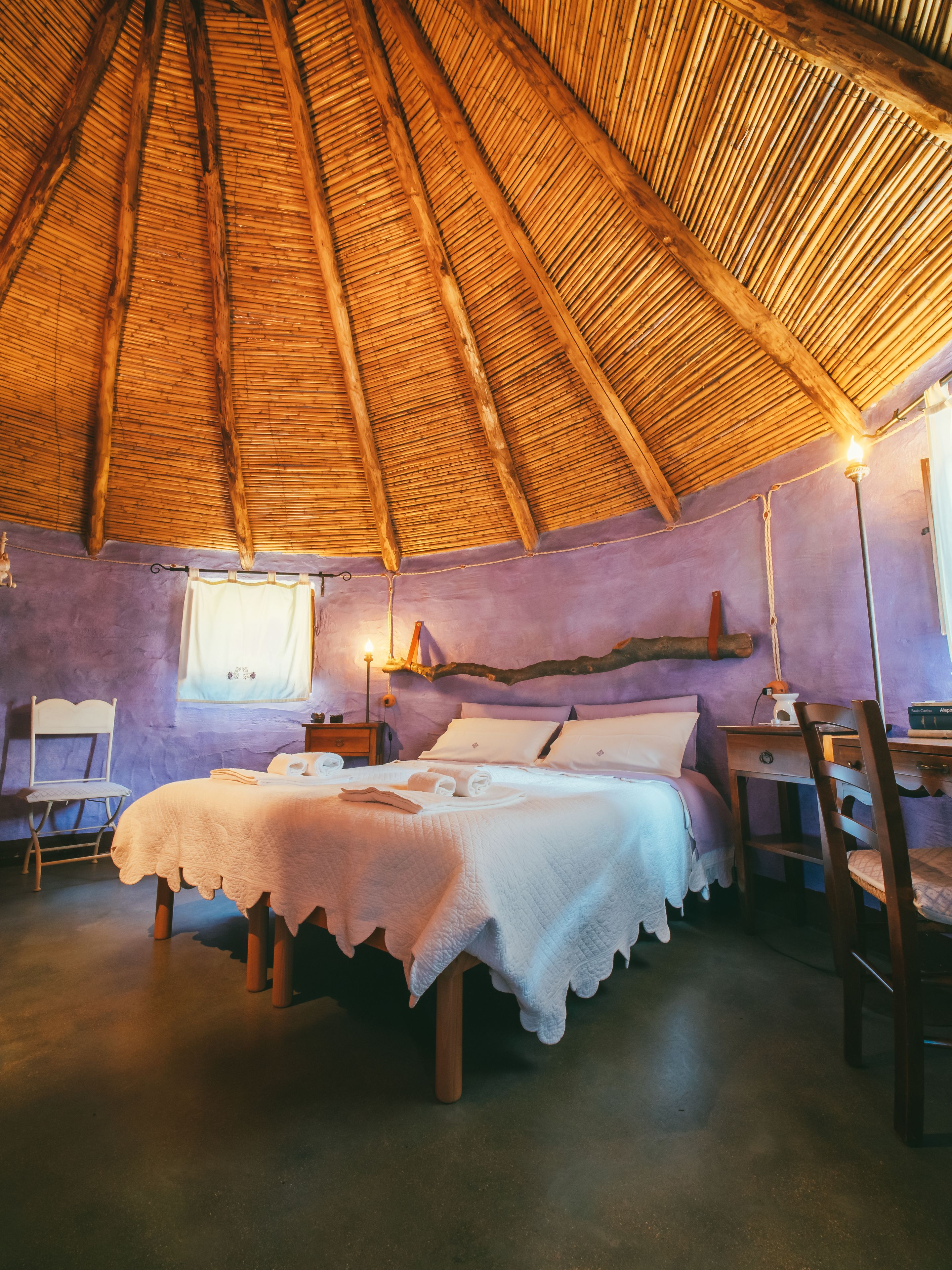 Een kamer met rieten dak, een bed met witte lakens, een tafeltje en een stoel.