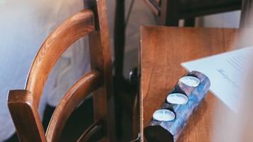 A wooden chair with a woven seat cushion, a wooden table with a tray holding a white object and a blue object, and a small white table lamp on a wooden nightstand.