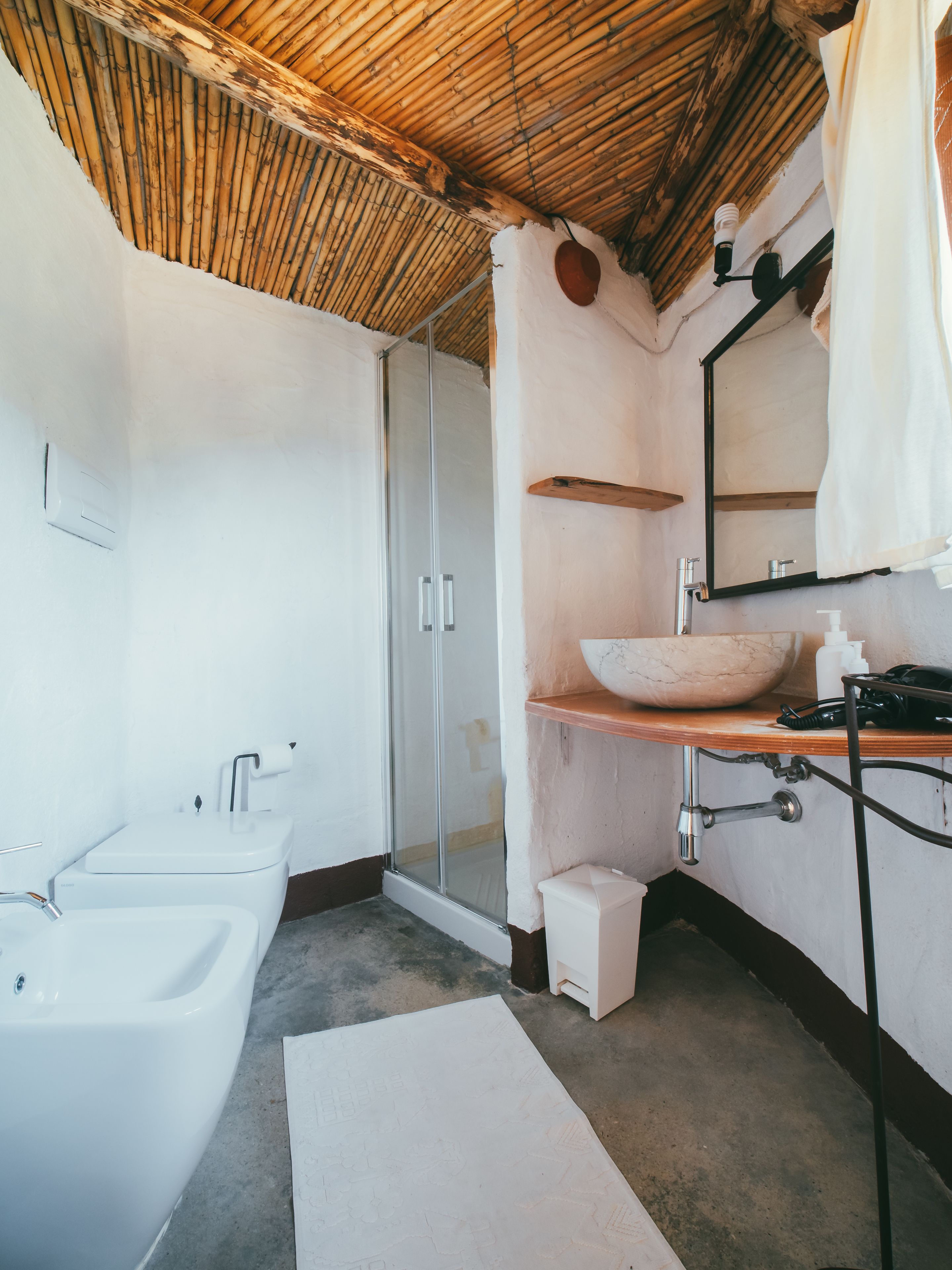 A bathroom with a large bathtub, a glass-enclosed shower, a wooden vanity with a marble basin, and a mirror with a towel hanging on the wall.