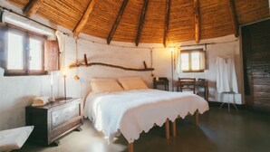 A cozy bedroom with a wooden ceiling, a bed with white linens, a dresser, and a small table with a chair. - Essenza Sardegna (Torpe)