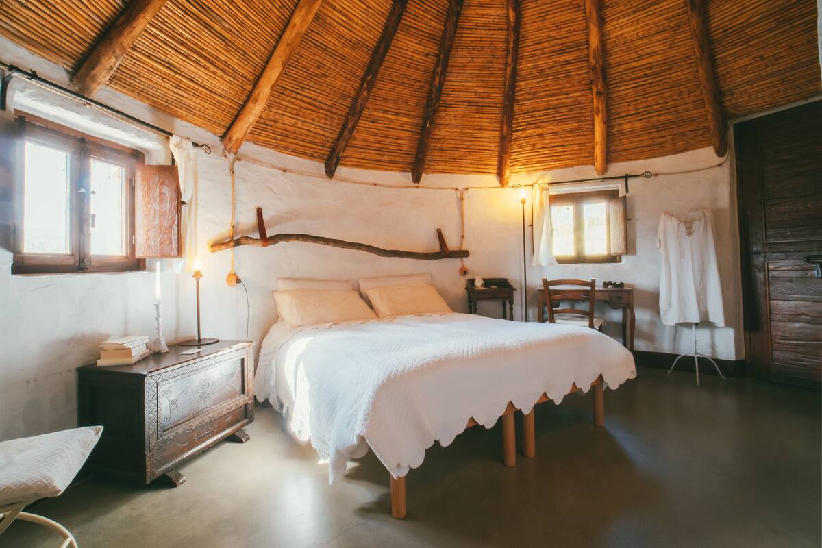 A cozy bedroom with a wooden ceiling, a bed with white linens, a dresser, and a small table with a chair.