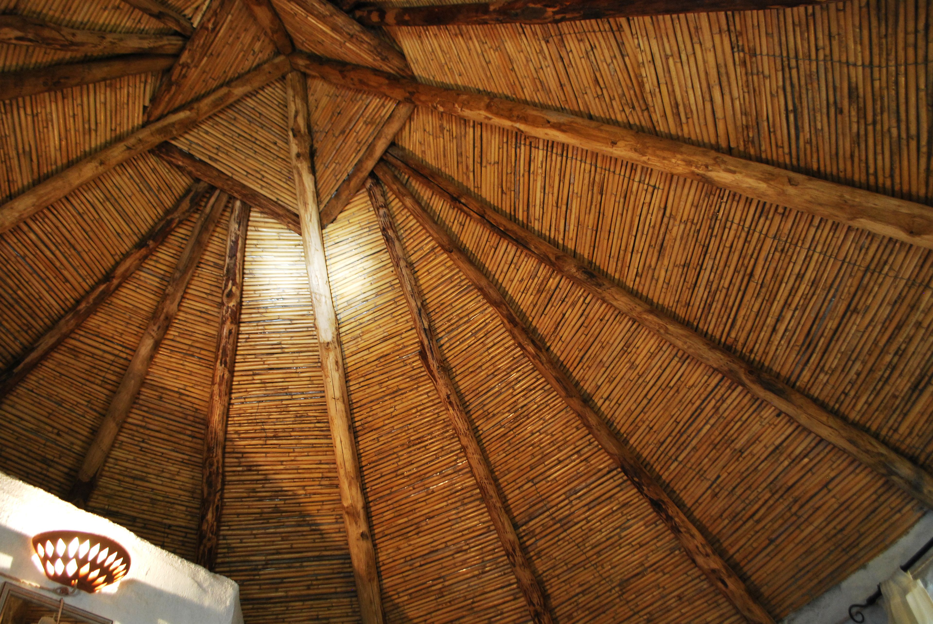 Estructura de techo de paja con vigas de madera y un accesorio de iluminación.