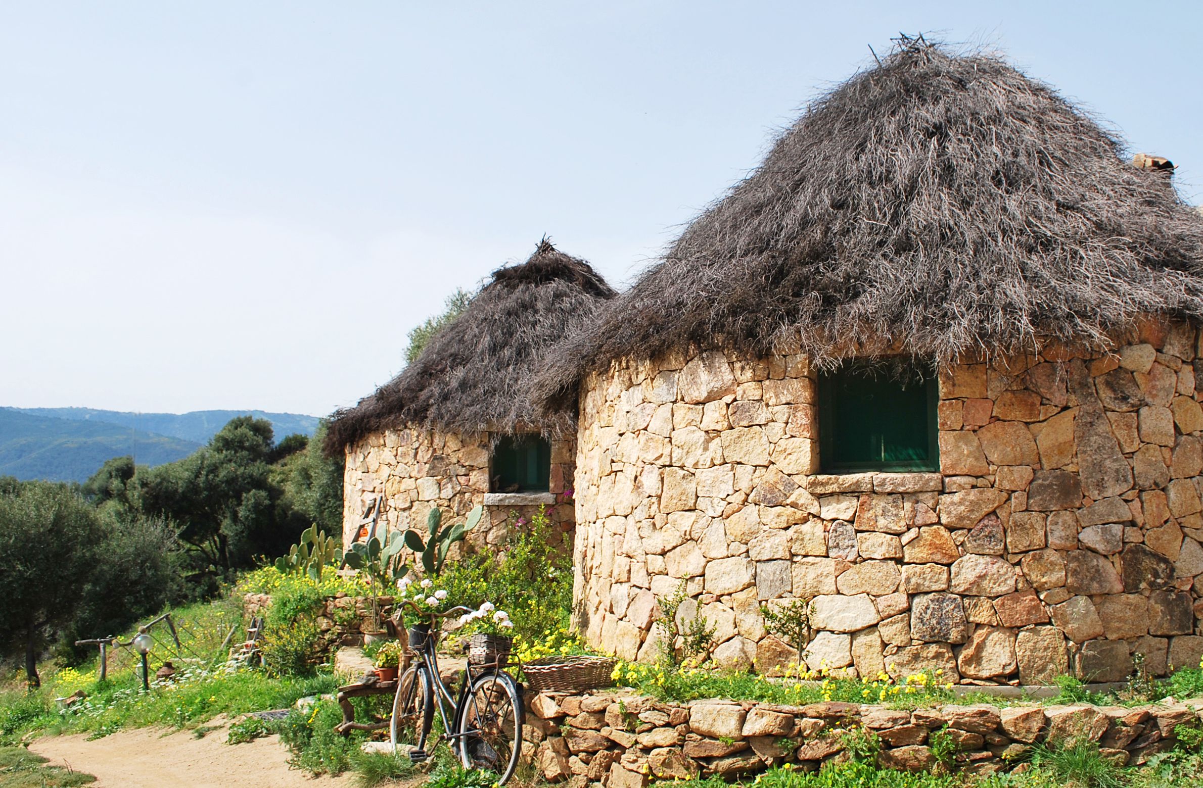 A stone house with a thatched roof and a bicycle parked outside.