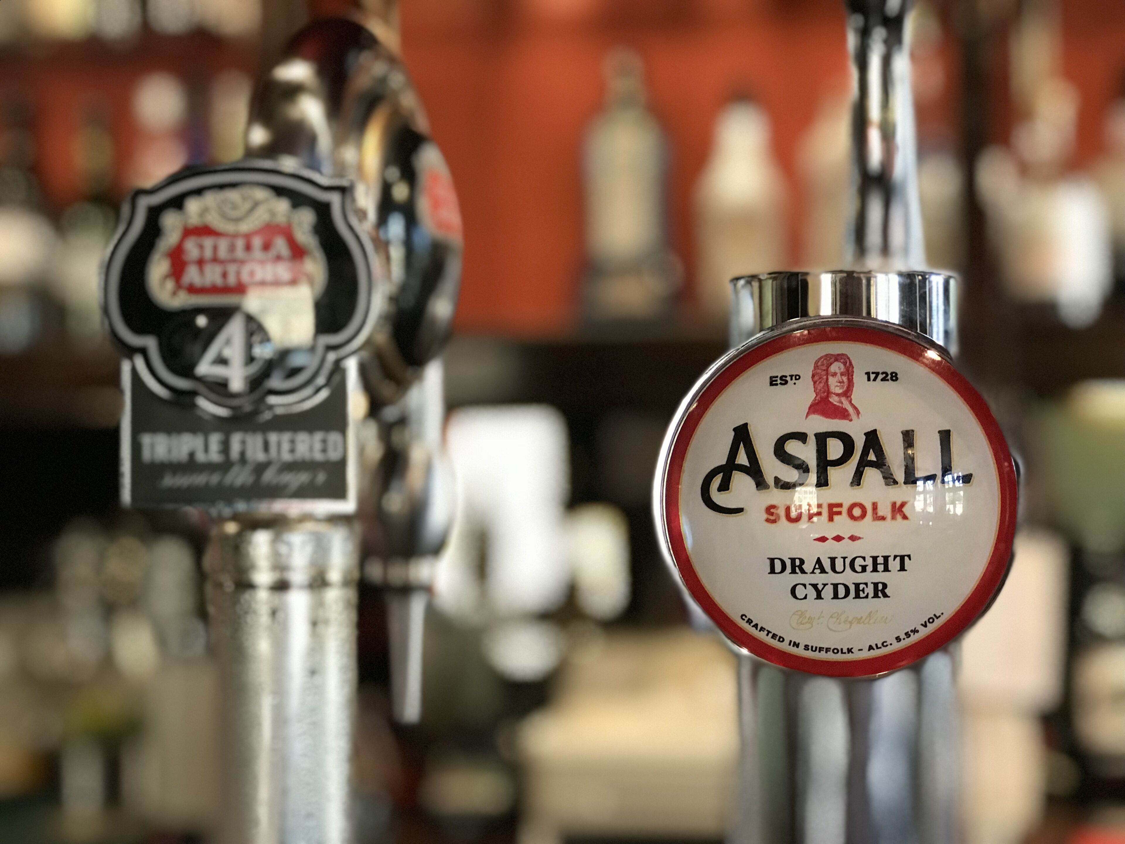 Un bar con dos grifos, uno etiquetado 'Stella Artois' y el otro 'Aspall Suffolk Draught Cider'.