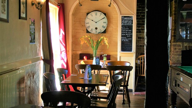 Ein Restaurantinnenraum mit einer Uhr, einer Speisekarte und einem Billardtisch.