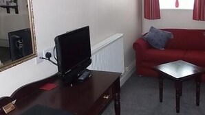 Ein Wohnzimmer mit Fernseher, einem roten Sofa, einem kleinen Tisch und einem Spiegel an der Wand.