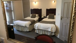 Ein Hotelzimmer mit zwei Einzelbetten, einem Schreibtisch, einem Stuhl und einem großen Spiegel.