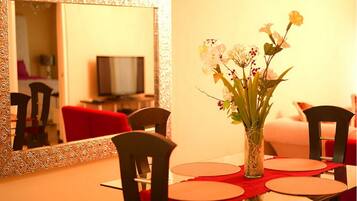 Un comedor con una mesa dispuesta para cuatro personas, un jarrón con flores y un espejo grande en la pared.