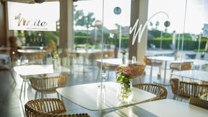 L’intérieur d’un restaurant avec des cloisons en verre, des chaises en osier et une table blanche agrémentée d’un vase de fleurs.