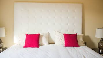 Una cama bien hecha con un cabecero capitonado, dos almohadas y dos lámparas de noche.