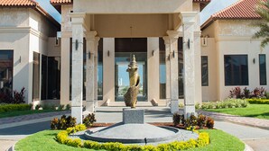 Un bâtiment doté d’une entrée centrale, d’une statue et d’un jardin aménagé.