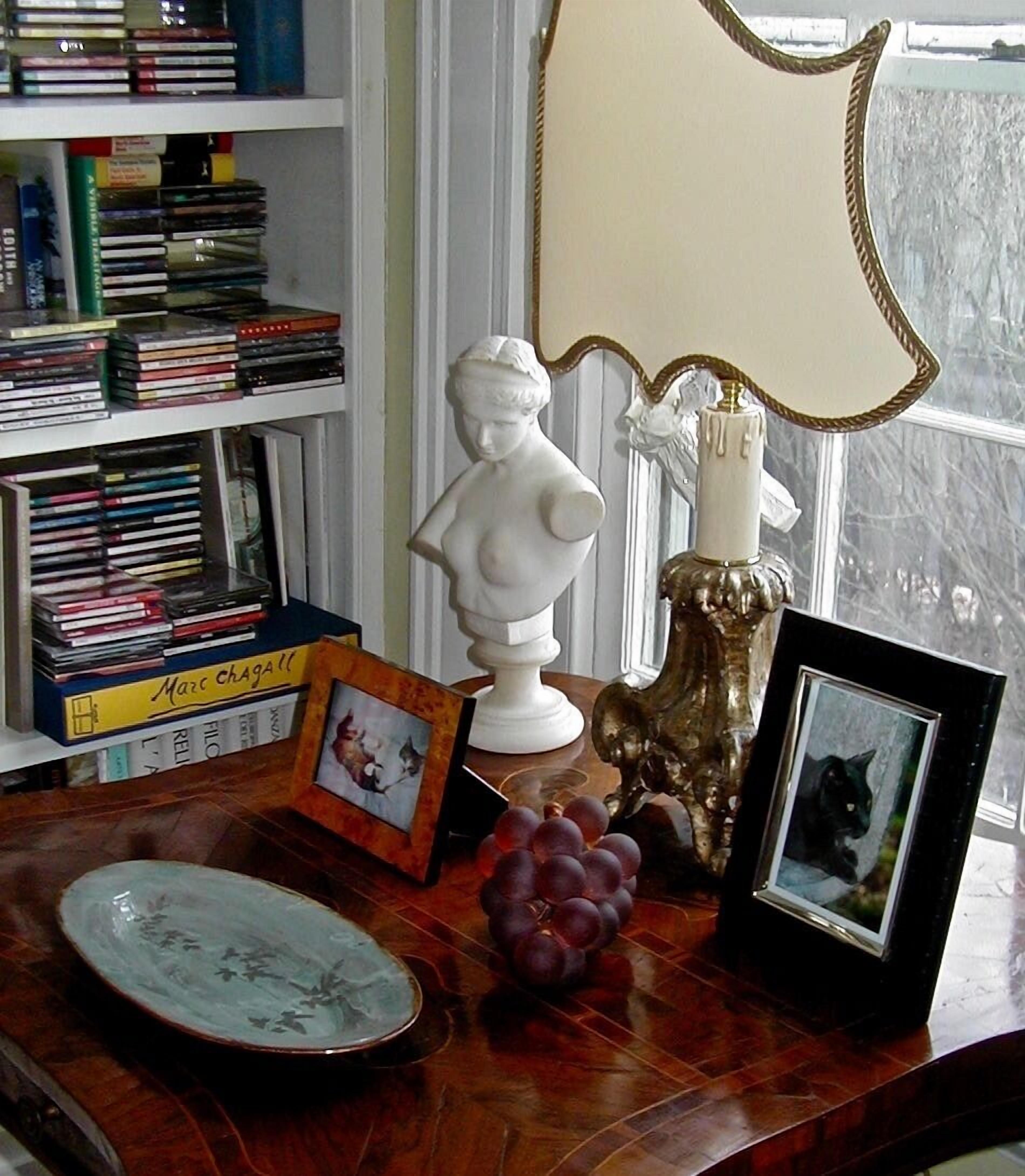 Una mesa de madera con un busto blanco, una fotografía enmarcada, un jarrón con uvas y un espejo decorativo.