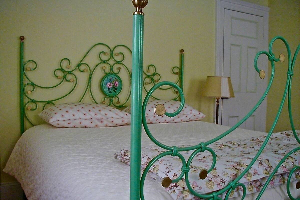 Un lit avec un cadre en métal vert, une literie à motifs floraux et une porte blanche en arrière-plan.