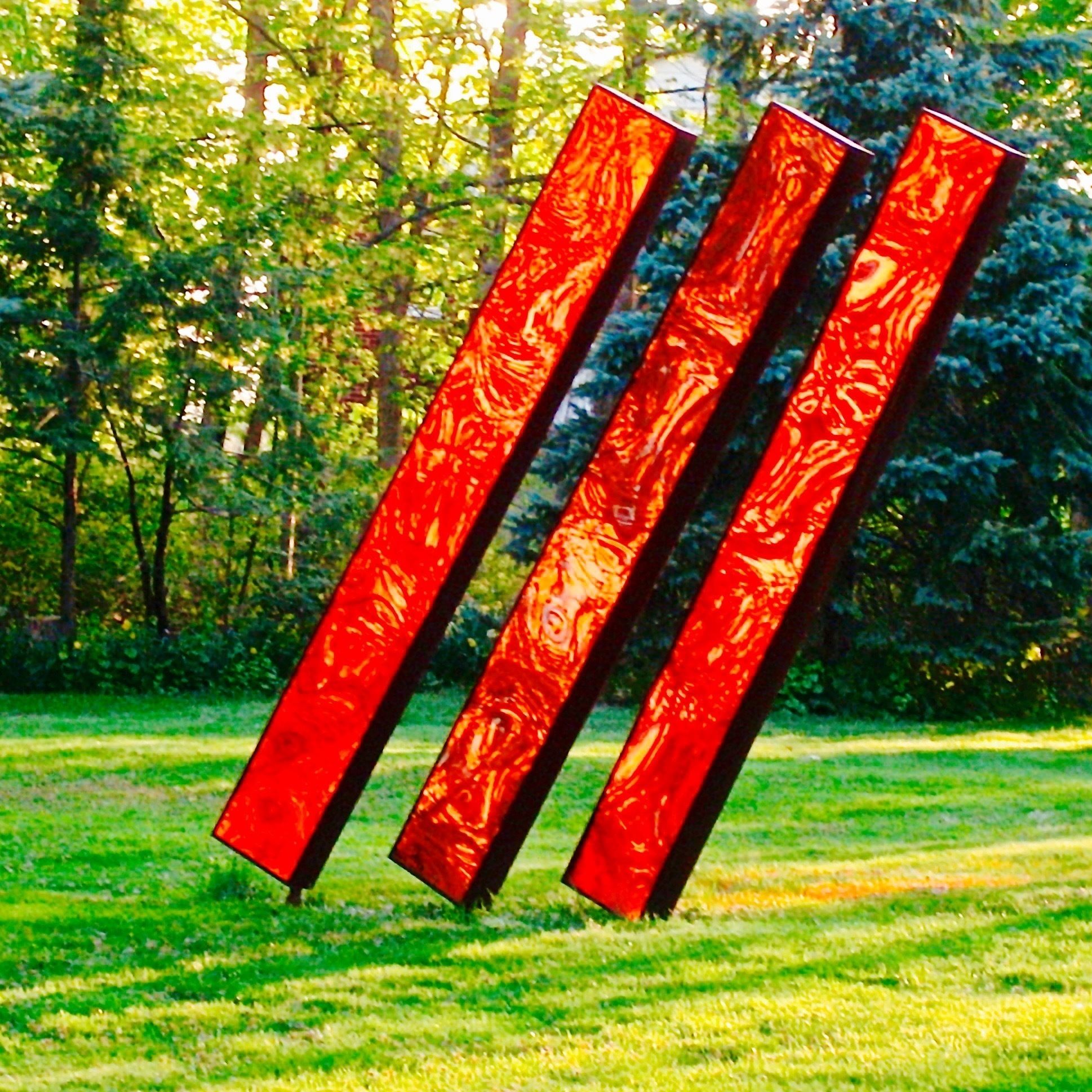 Three vertical red panels in an outdoor setting with green grass and trees in the background.