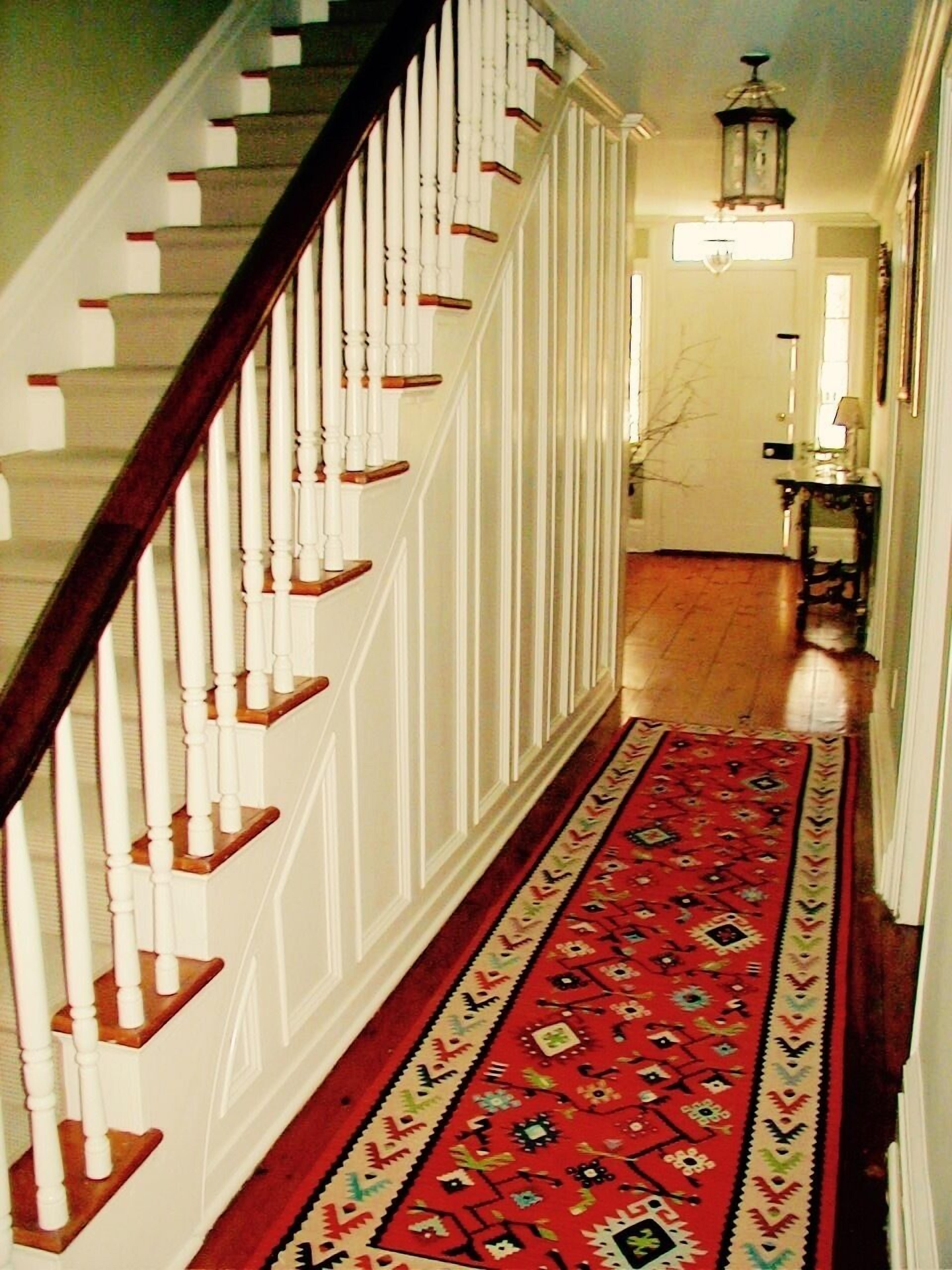 A staircase with white railings and wooden steps leading to a hallway with a patterned carpet.