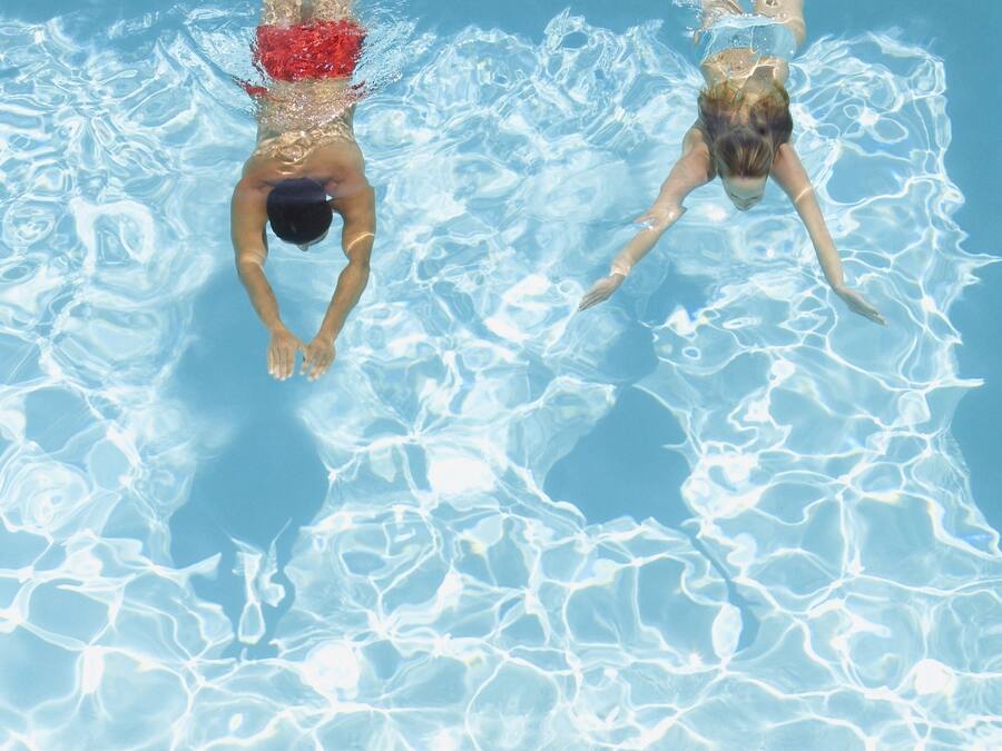 Een zwembad met helder water en twee zwemmers.