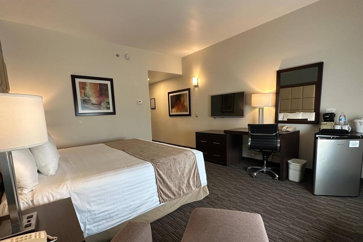 Ein Hotelzimmer mit Bett, Schreibtisch, Stuhl und einem kleinen Kühlschrank.