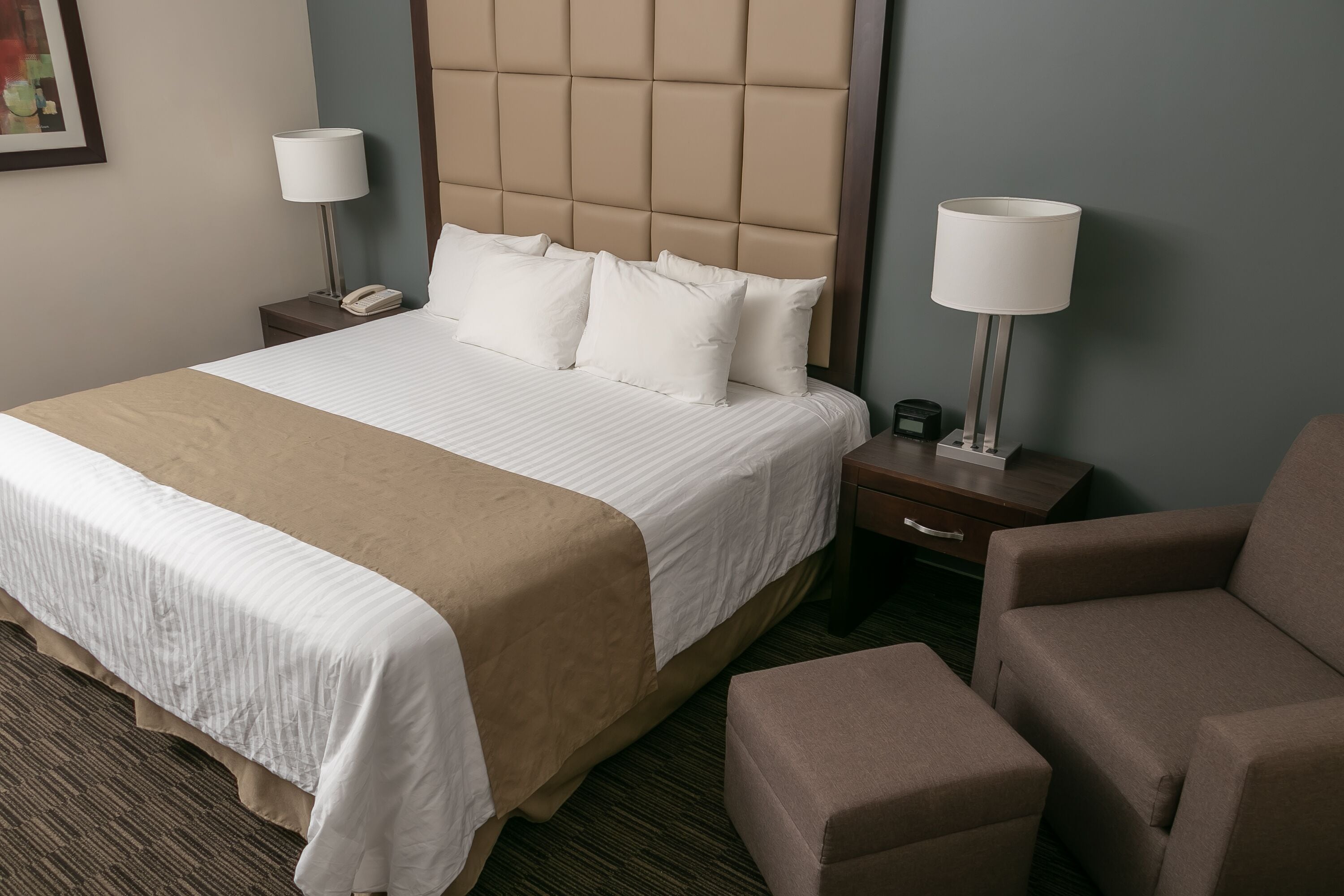 Una habitación de hotel con una cama grande, dos mesitas de noche, una silla y una pequeña mesa.