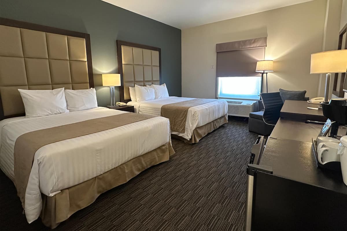 Ein Hotelzimmer mit zwei Betten, einem Schreibtisch, einem Stuhl, einer Lampe und einem Fenster.
